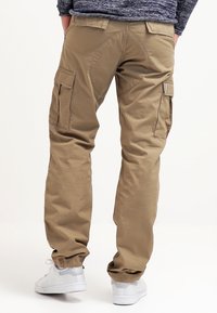 Pantaloni cargo beige con tasche laterali, caratterizzati da una vestibilità comoda e polsini elastici. Tessuto leggermente testurizzato, con un'etichetta del marchio ben visibile sul retro.