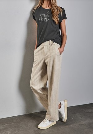 Sort t-shirt med korte ærmer og hvid tekst "SPARK FOUND," kombineret med beige brede bukser med striber og hvide sneakers.