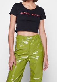 Camiseta negra corta con texto rojo "MISS SIXTY", combinada con pantalones de vinilo verdes brillantes de cintura alta. Presenta mangas cortas y un cuello redondo.
