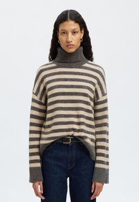 Gestreifter Rollkragenpullover in Beige und Grau, oversized geschnitten mit geripptem Kragen und Ärmeln, aus weichem Strickmaterial gefertigt. Getragen mit dunklen Jeans.