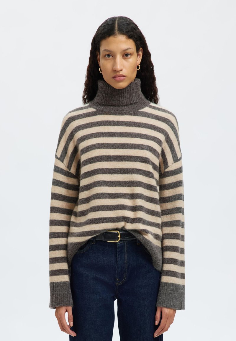 Gestreifter Rollkragenpullover in Beige und Grau, oversized geschnitten mit geripptem Kragen und Ärmeln, aus weichem Strickmaterial gefertigt. Getragen mit dunklen Jeans.