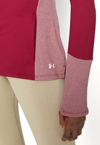 Långärmad atletisk top med en vinröd kropp och ljusare vinröda ärmar, flatlock-sömmar och en liten vit logotyp nära fållen.