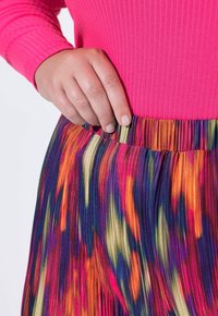 Top rosa ajustado de canalé combinado con una falda de pliegues colorida que presenta vibrantes patrones en rosa, naranja, púrpura y crema.