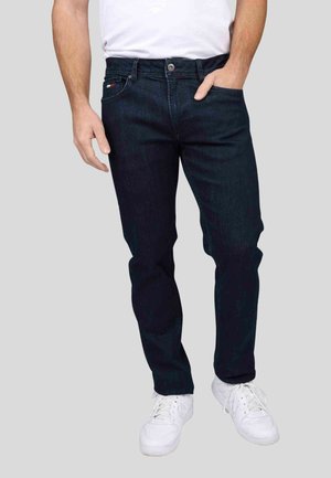 Jean en denim bleu foncé avec une coupe droite, présentant un design classique à cinq poches et une fermeture à bouton. Associé à des baskets blanches.