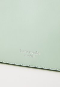 Mint green leather wallet with embossed "kate spade NEW YORK" logo. Features smooth texture and fine white stitching along edges.