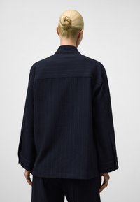 Giacca oversize in blu navy, con texture, colletto, maniche lunghe e dettagli con bottoni, che presenta un sottile motivo a righe.