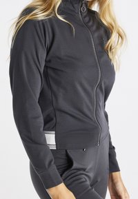 Ciemnoszara kurtka na zamek z wysokim kołnierzem, dopasowanym krojem i subtelnymi paskami po bokach. Miękka tkanina i gładka faktura.