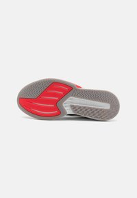 Semelle de chaussure de sport noire avec des accents rouges proéminents, surface de grip texturée et une section surélevée portant le logo "LIGHTSTRIKE".