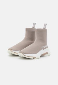 Botas de tobillo beige con parte superior de punto, suela blanca y acentos texturizados. Presenta el logo "STEVE MADDEN" en el costado y una lengüeta de tirón.
