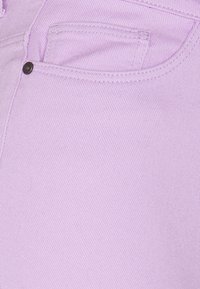 Jeans de color púrpura claro con un acabado texturizado, que presentan un bolsillo delantero y un pequeño detalle de botón negro.