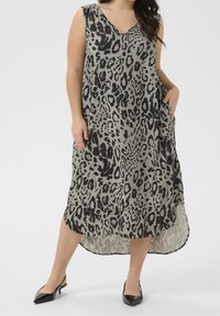 Femme taille plus portant une robe midi sans manches à imprimé léopard avec un ourlet asymétrique et des escarpins noirs à talon ouvert.