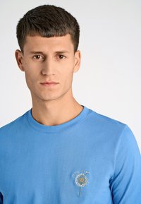 Ljusblå långärmad t-shirt i bomull med en maskros-broderidesign och rundad halsringning. Enkel och avslappnad look.