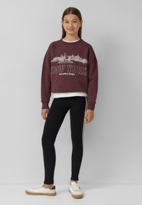 Bordowy, krótki sweatshirt z nadrukiem "NEW YORK", zestawiony z czarnymi legginsami z bocznymi paskami i białymi trampkami z beżową podeszwą.