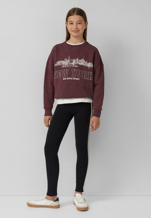 Bordowy, krótki sweatshirt z nadrukiem "NEW YORK", zestawiony z czarnymi legginsami z bocznymi paskami i białymi trampkami z beżową podeszwą.