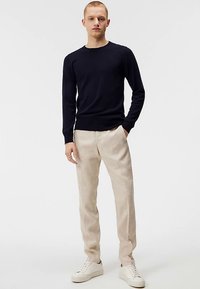 Mörkblå stickad tröja med rund halsringning, kombinerad med ljusbeige linnebyxor och vita sneakers, stylad casual.