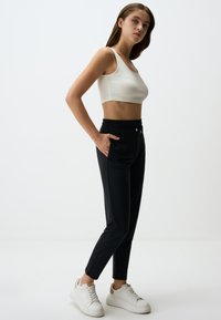 Schwarze Sporthose mit elastischem Bund, seitlichen Taschen und glatter Textur, kombiniert mit einem weißen gerippten Crop-Top und weißen Sneakern.