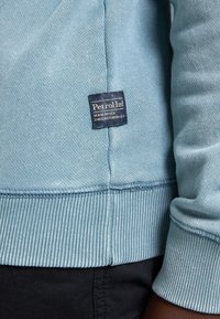 Felpa azzurra con polsini e orlo a coste. Presenta un'etichetta tessuta che recita "Petrol Ind Denim Driven" vicino alla cucitura.