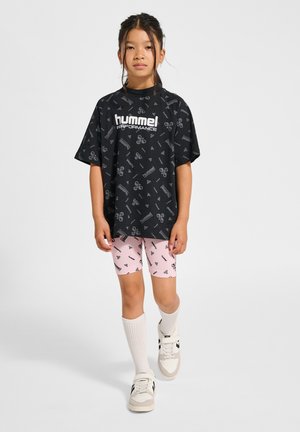 Czarny, oversize t-shirt z białym logo i wzorami, w połączeniu z różowymi szortami rowerowymi z powtarzającymi się czarnymi wzorami, białymi skarpetkami i sneakerami.