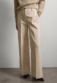 Helle beiger Corduroy-Weitbeinhosen mit vorderen Falten und glatter Textur, kombiniert mit einem gestrickten Pullover und dunklen Absätzen.