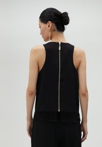Čierny top bez rukávov so zipsom na chrbte, zdobený frnžou z korálkov pozdĺž lemu a hladkou, matnou textúrou.