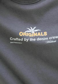 Harmaa puuvillapaita, jossa on rohkea oranssi teksti "ORIGINALS" ja valkoinen teksti "Crafted by the denim crew" sekä "SAN FRANCISCO."