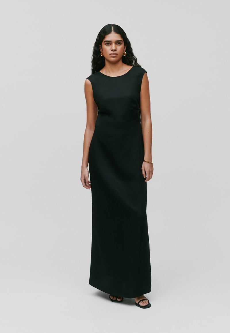 Melnā bez piedurknēm maksī kleita, elegants dizains, gluda tekstūra, taisna silueta, apaļa kakla izgriezums, valkāta ar vienkāršām melnām sandālēm.