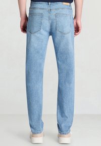 Jeans in denim azzurro chiaro con taglio dritto, con due tasche posteriori e cuciture minime. Indossati con sneakers bianche.