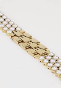 Pulsera en tono dorado que presenta enlaces dorados lisos alternando con cuentas similares a perlas. El diseño es elegante y moderno, con un brillo sofisticado.