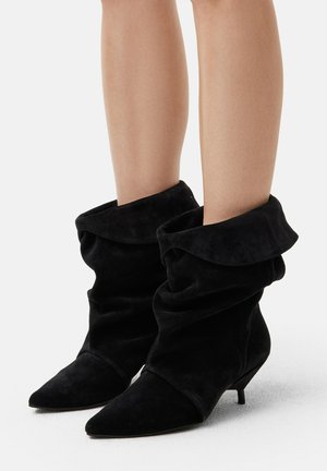 Bottes noires en daim à chevilles avec un design décontracté, bout pointu et un détail de revers. Le talon est de style kitten, bas et fin.