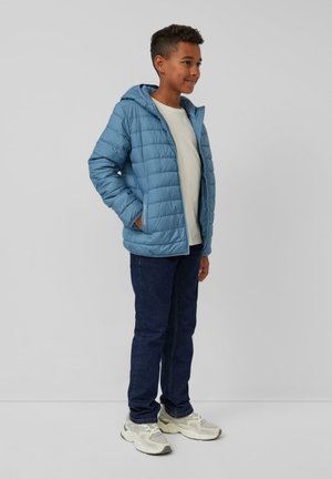 Lichtblauwe gewatteerde hooded jas met twee zijzakken, gedragen over een wit shirt en gecombineerd met donkere jeans en grijze sneakers.