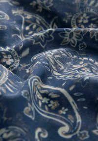 Tumesinine kangas, millel on kreemi ja beeži toonides lilleline paisley muster; kerge tekstuur, millel on peened detailid ja pehme lange.