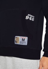 Felpa nera con tasca frontale, con la scritta "since 948" stampata in argento, e un'etichetta tessuta che mostra i dettagli NBA e del marchio.