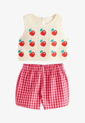 Top in crochet senza maniche color crema con motivi di mele rosse abbinato a pantaloncini a vita elastica in tessuto a quadretti rosa e rossi.