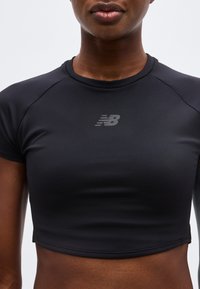 Κοντινό πλάνο ενός ατόμου που φοράει εφαρμοστή μαύρη κοντή αθλητική μπλούζα με γκρι λογότυπο New Balance στο στήθος.