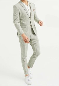 Ljust grå rutigt kostym med skräddarsydd passform, har en enfärgad kavaj och smala byxor, kombinerat med en vit polo och vita sneakers.