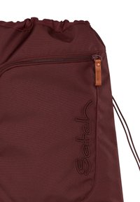 Maroon drawstring bag with a gathered top, featuring a side zip pocket and stitched logo detail. Made from durable fabric with a smooth texture.