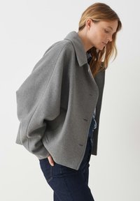 Giacca in misto lana grigia con una silhouette strutturata, ampio colletto e maniche oversize. Chiusura con bottoni, presenta una finitura testurizzata.