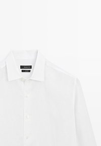 Chemise blanche en lin à manches longues avec col classique et boutons, étiquetée Massimo Dutti, présentée sur un fond blanc.