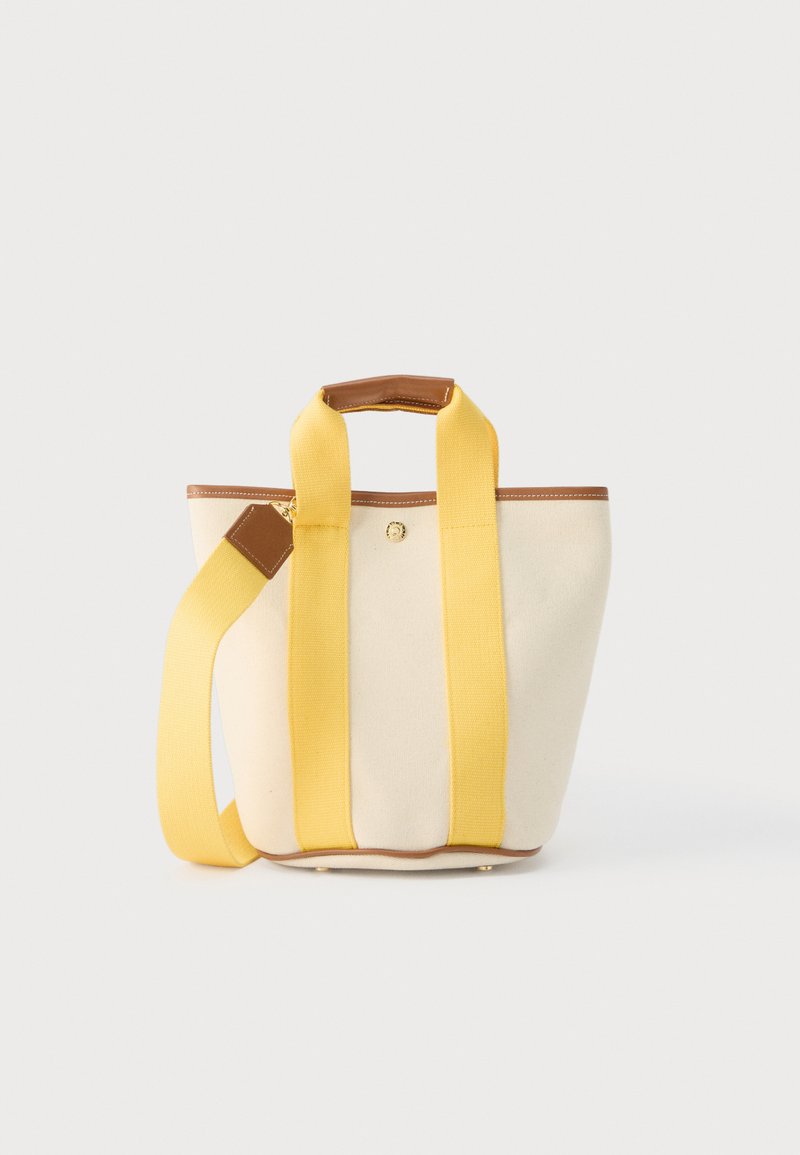 Τσαντάκι ώμου από καμβά σε κρεμ χρώμα με φαρδιές κίτρινες τιράντες, καφέ δερμάτινη επένδυση και αποσπώμενο ιμάντα ώμου, σε ανοιχτό φόντο.