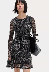 Abito nero con maniche lunghe in organza, caratterizzato da un motivo testurizzato di forme bianche e grigie. Gonna svasata con vita elastica, abbinata a una borsa nera.