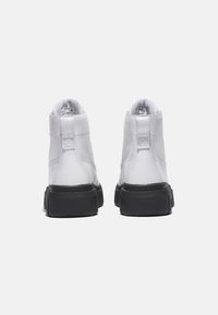 Baskets montantes blanches avec un dessus en cuir lisse et une semelle en caoutchouc noire. Présente un col rond, une petite languette à l'arrière et des détails de couture minimaux.