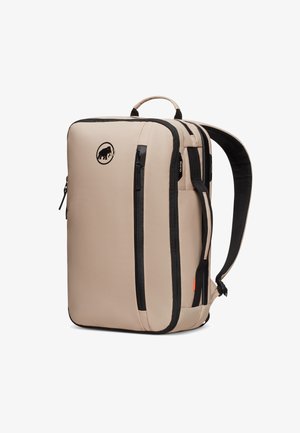 Sac à dos beige de forme rectangulaire, avec des zips noirs et un logo. Il dispose d'une poignée supérieure et de bretelles rembourrées pour plus de confort.