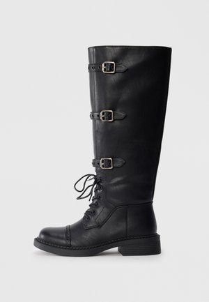 Schwarze Lederstiefel bis zum Knie mit Schnürung an der Vorderseite, drei Schnallenakzenten, runder Zehenform und niedrigem Blockabsatz. Glatte Textur mit matter Oberfläche.