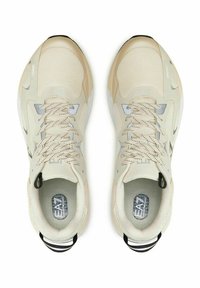 Un paio di sneaker beige e grigio chiaro con lacci, dotate di pannelli in rete e anelli neri sul tallone, viste dall'alto su uno sfondo bianco.