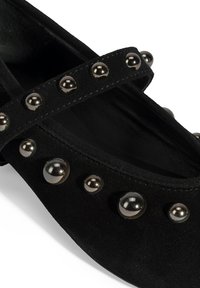 Schwarze Wildleder-Flachschuhe mit einem gekreuzten Riemen und metallischen Perlenakzenten entlang der oberen Kante und Seiten. Glatte Innenauskleidung.
