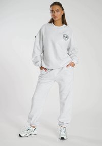 Grijze oversized sweatshirt met een ronde hals en zwarte grafische print op de borst, gecombineerd met bijpassende grijze joggers en sneakers.