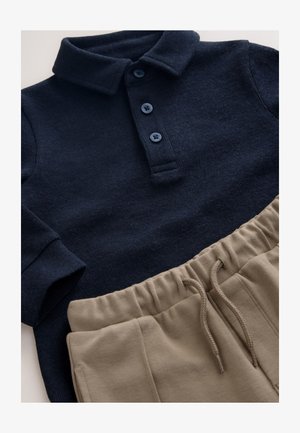 Námornícky modrý pulóver s textúrovanou látkou a predným zapínaním na tri gombíky, doplnený béžovými šortkami so elastickým pásom, bočnými vreckami a sťahovacou šnúrkou.