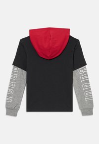 T-shirt noir avec capuche rouge et manches longues grises. Les manches grises présentent un texte blanc le long de leur longueur. Matière en coton doux.