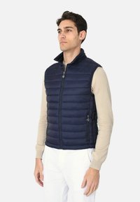 Gilet imbottito leggero di colore blu navy con colletto alto, zip anteriore e due tasche laterali con chiusura a zip. Texture liscia e design trapuntato.