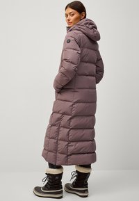 Cappotto lungo, morbido, color malva con cappuccio, design a righe orizzontali e tasca laterale. Abbinato a stivali invernali neri foderati in pelliccia.
